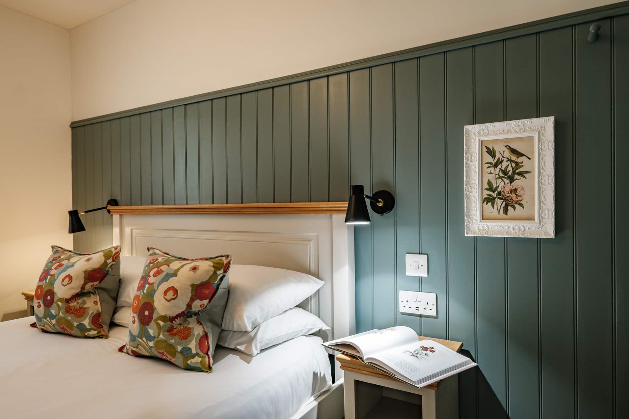 Casa 23 bedroom detail with sage panelling, floral cushions and framed bird print at Douneside House