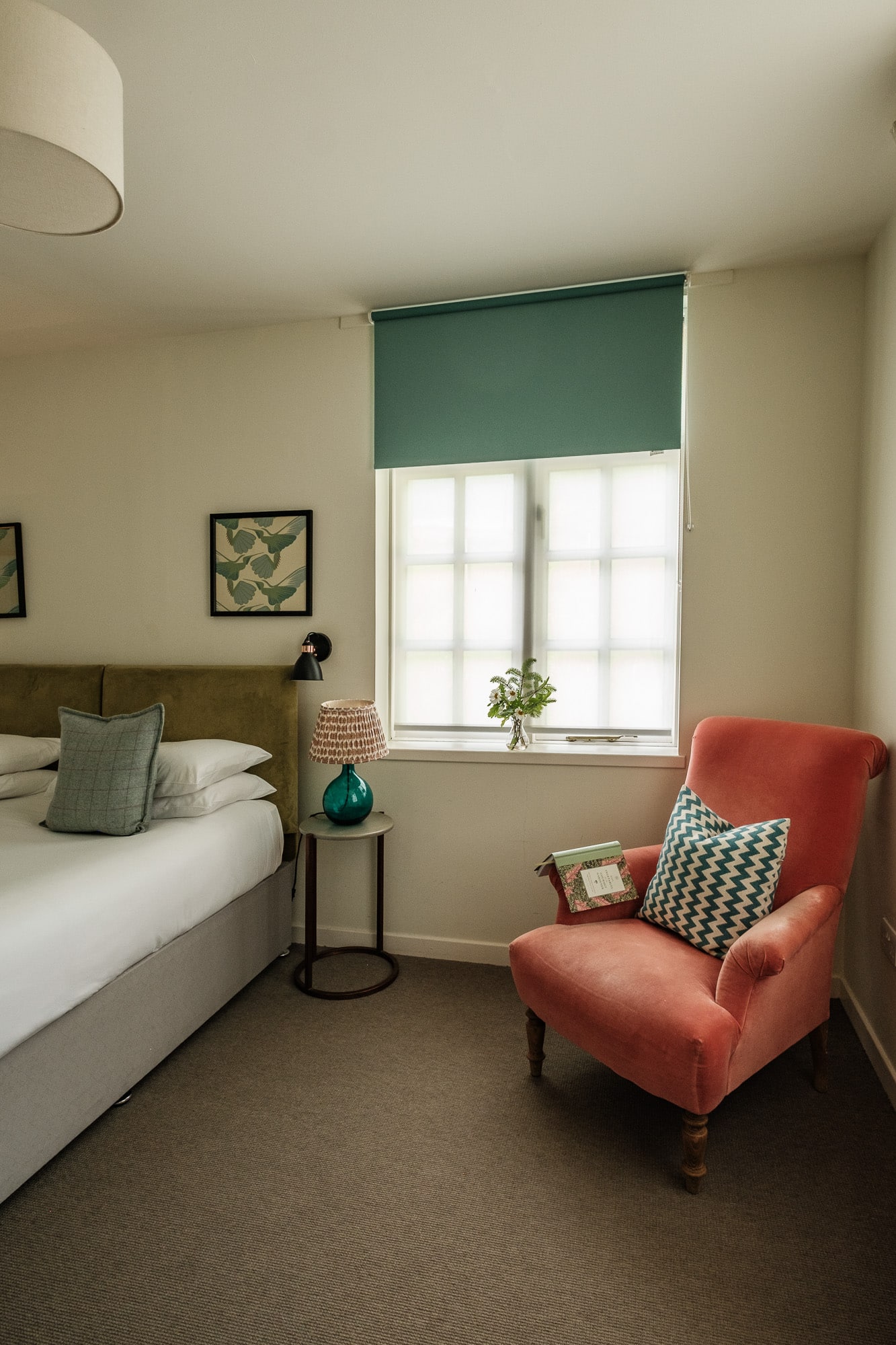 Morven Cottage bedroom with olive velvet headboard, coral reading chair and teal window blind at Douneside House