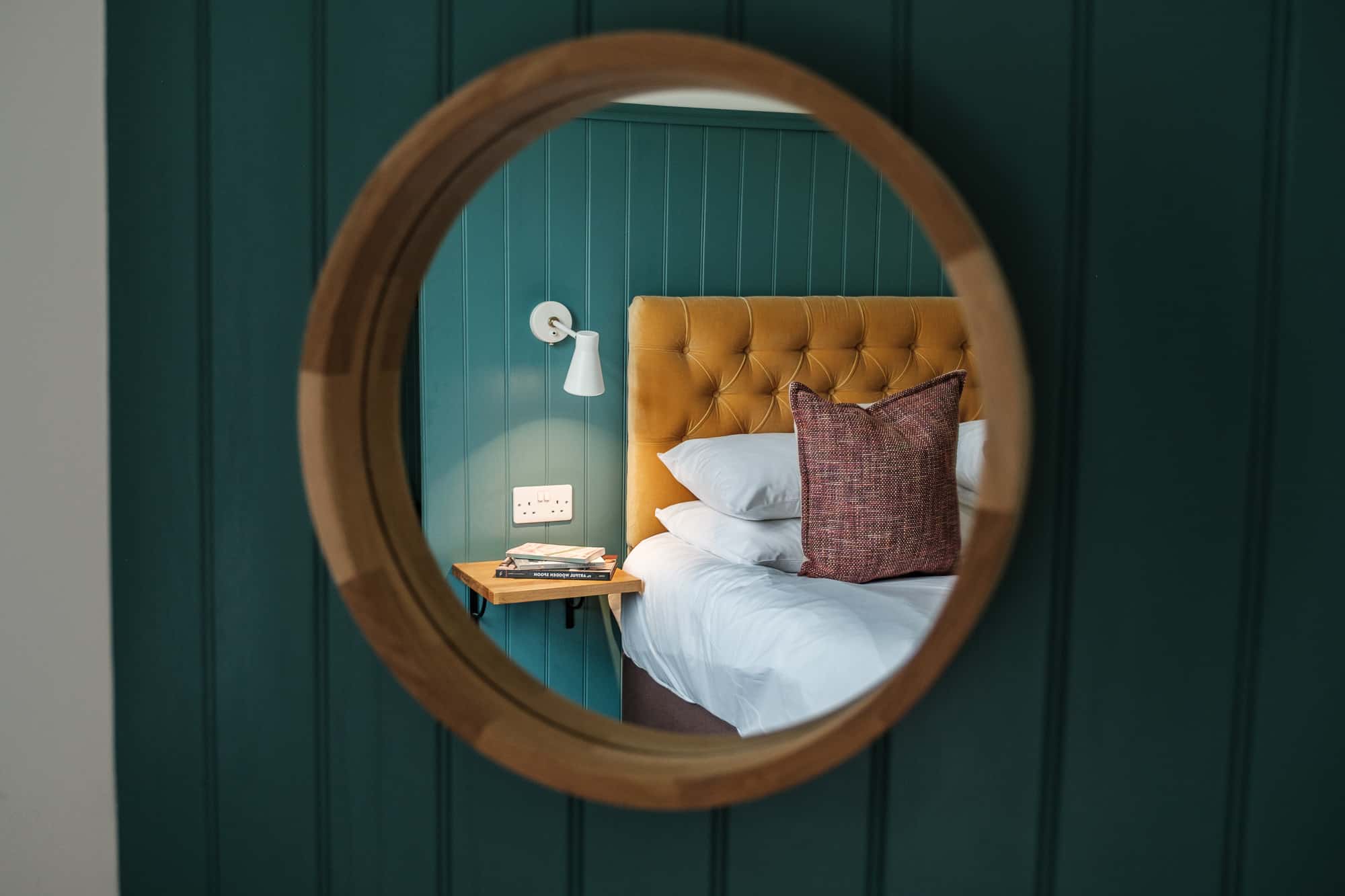 Bedroom_Through_Mirror_Dounebrae_Cottage Dounebrae Cottage bedroom viewed through round oak mirror with mustard velvet headboard and teal panelling at Douneside House
