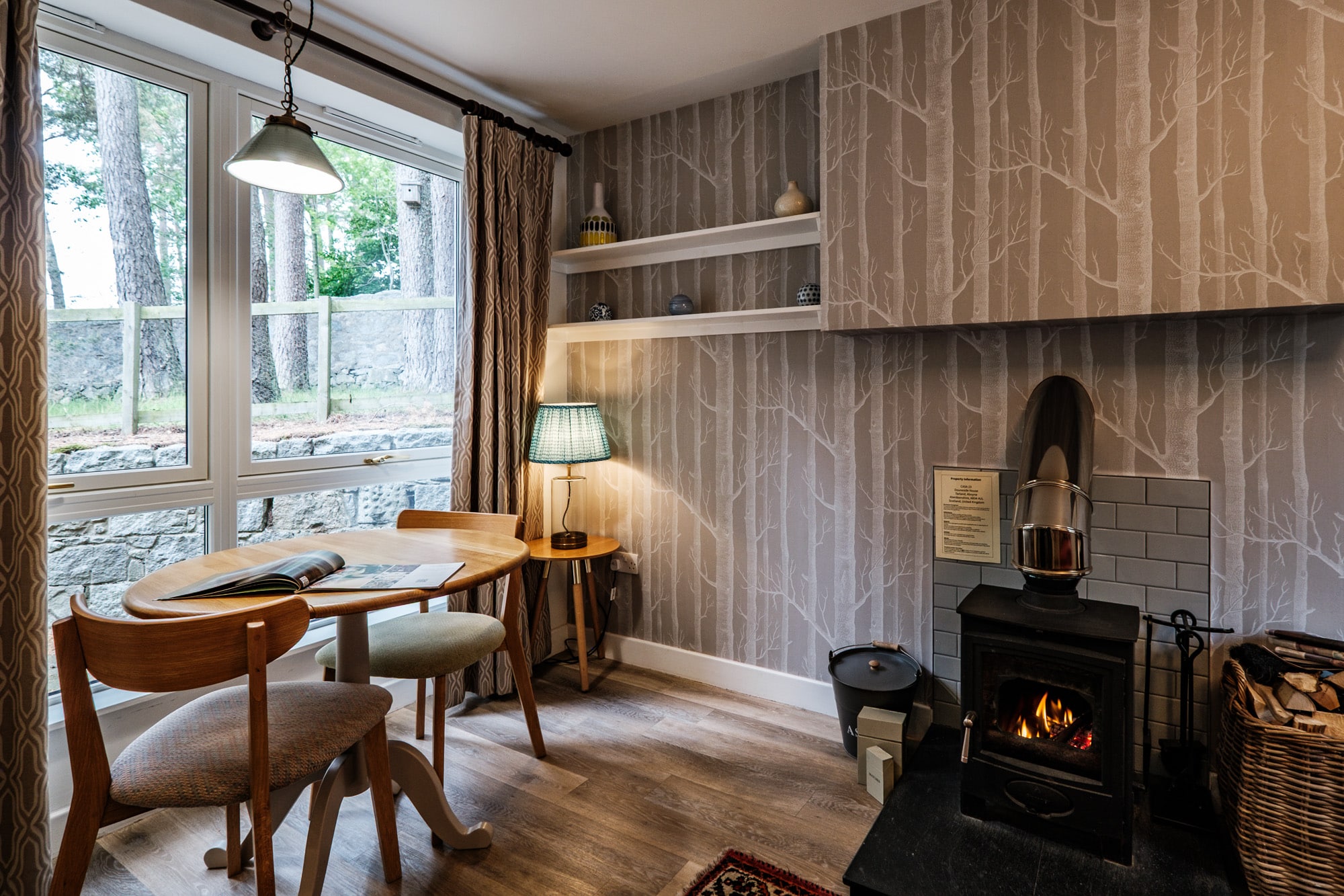 Casa 23 dining nook with round table beside wood-burning stove and birch tree wallpaper at Douneside House