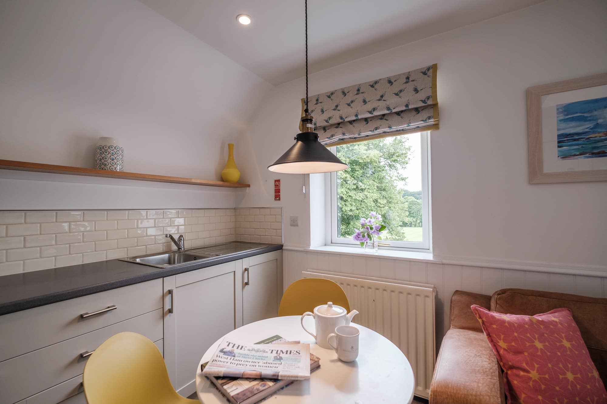 Casa 24 dining table with yellow chairs, tan leather sofa and hummingbird-print blind at Douneside House