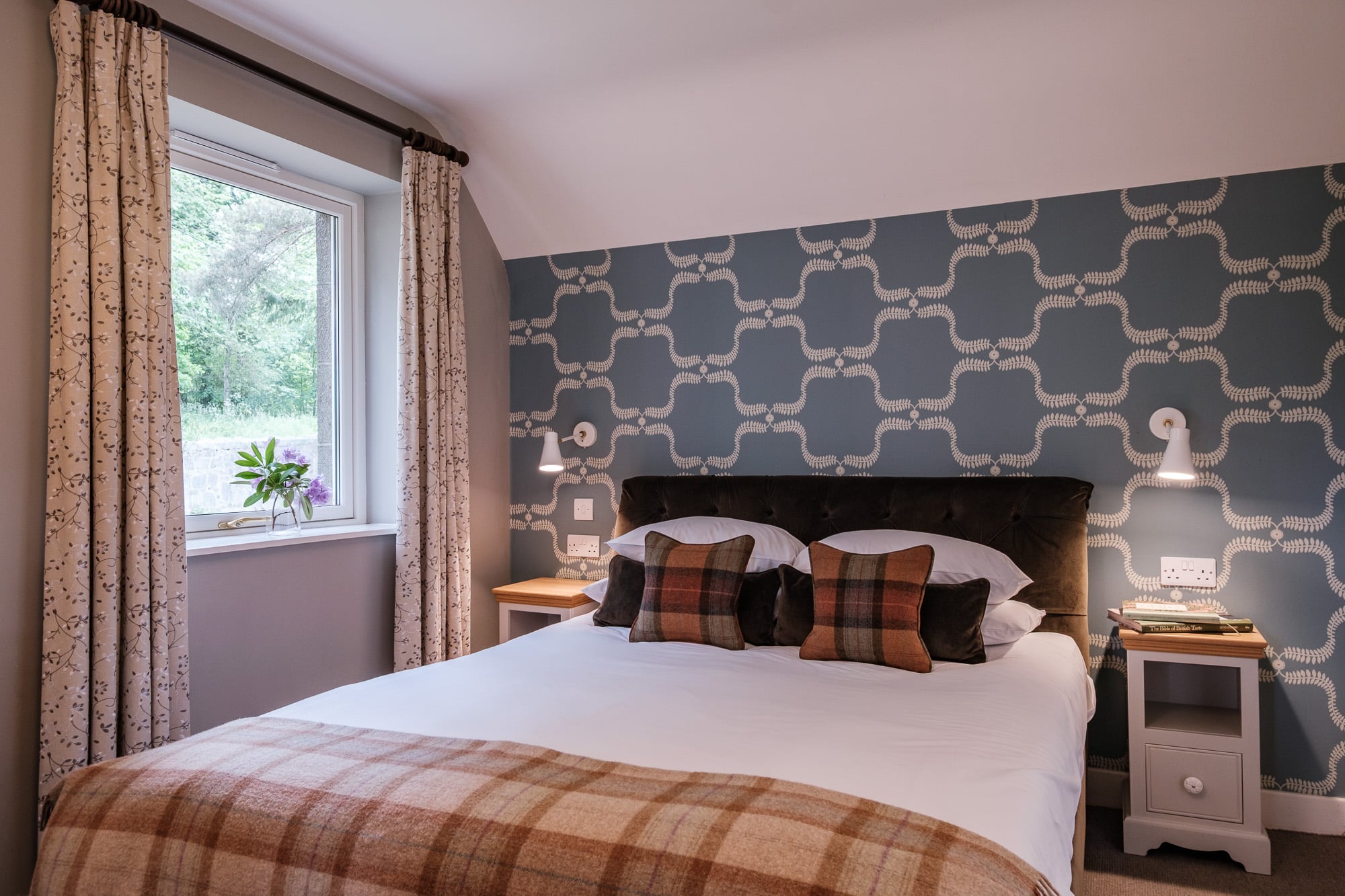 Double bedroom in Casa 24 with velvet headboard, tartan cushions and blue patterned wallpaper at Douneside House
