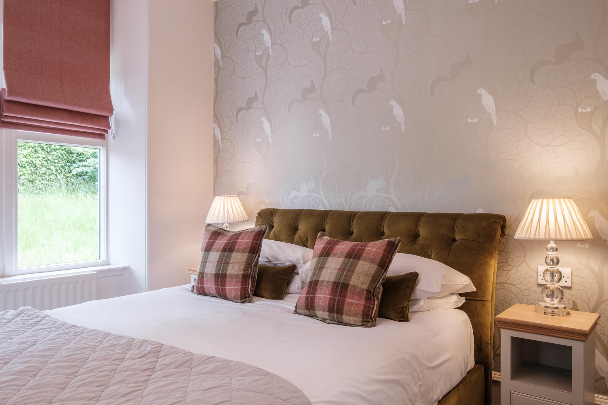 Double bedroom in Gatehouse with velvet headboard, bird print wallpaper and tartan cushions at Douneside House