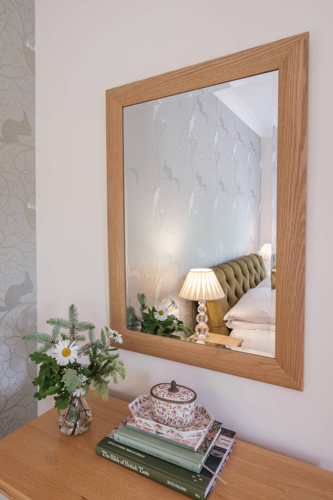 Gatehouse bedside detail with oak-framed mirror, wildflowers and country books at Douneside House