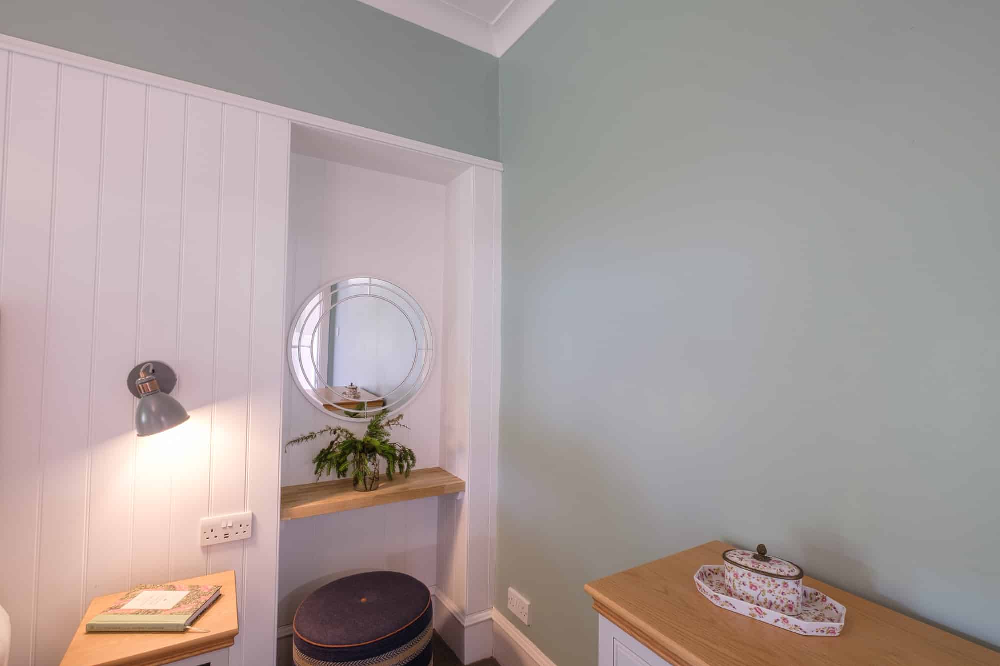 Gatehouse dressing area with round mirror, panelled niche and sage green walls at Douneside House