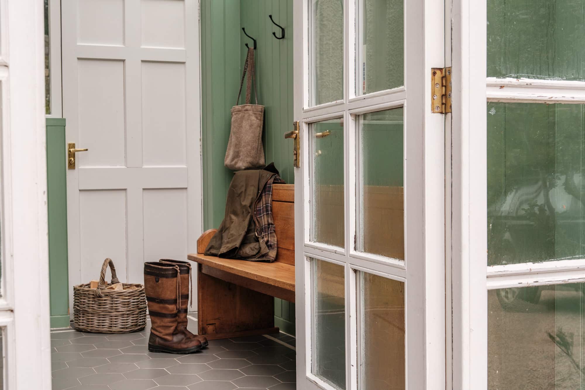 Glazed porch entrance to Casa 23 with sage panelling, oak pew and hexagonal tile floor at Douneside House