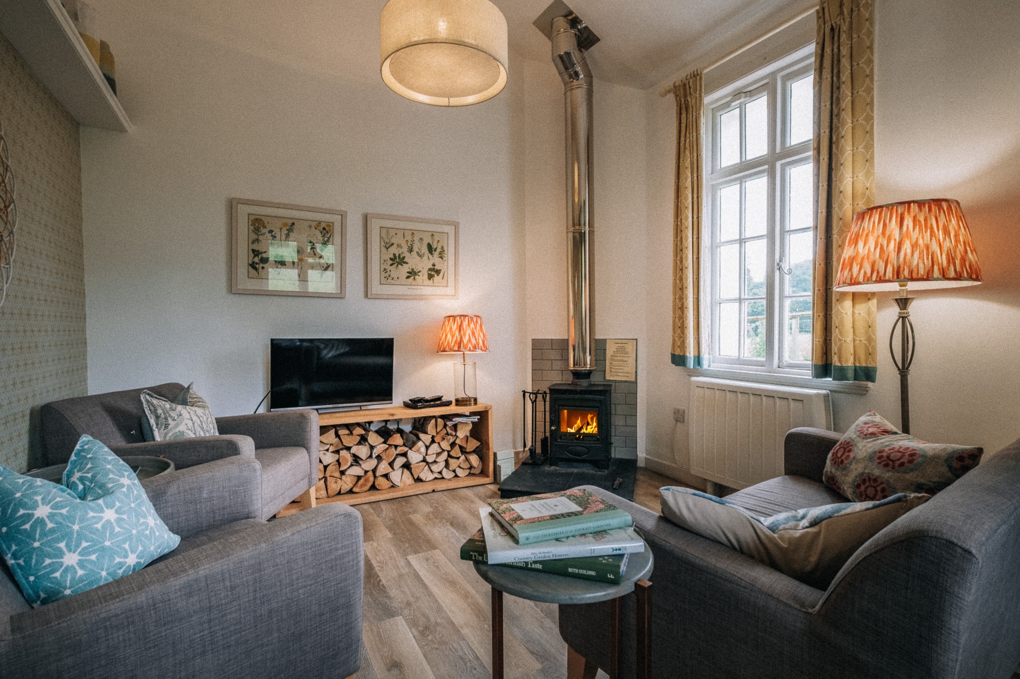 Fireside_Detail_Dounebrae_Cottage Living room in Dounebrae Cottage with wood-burning stove, log store, grey sofas and botanical prints at Douneside House