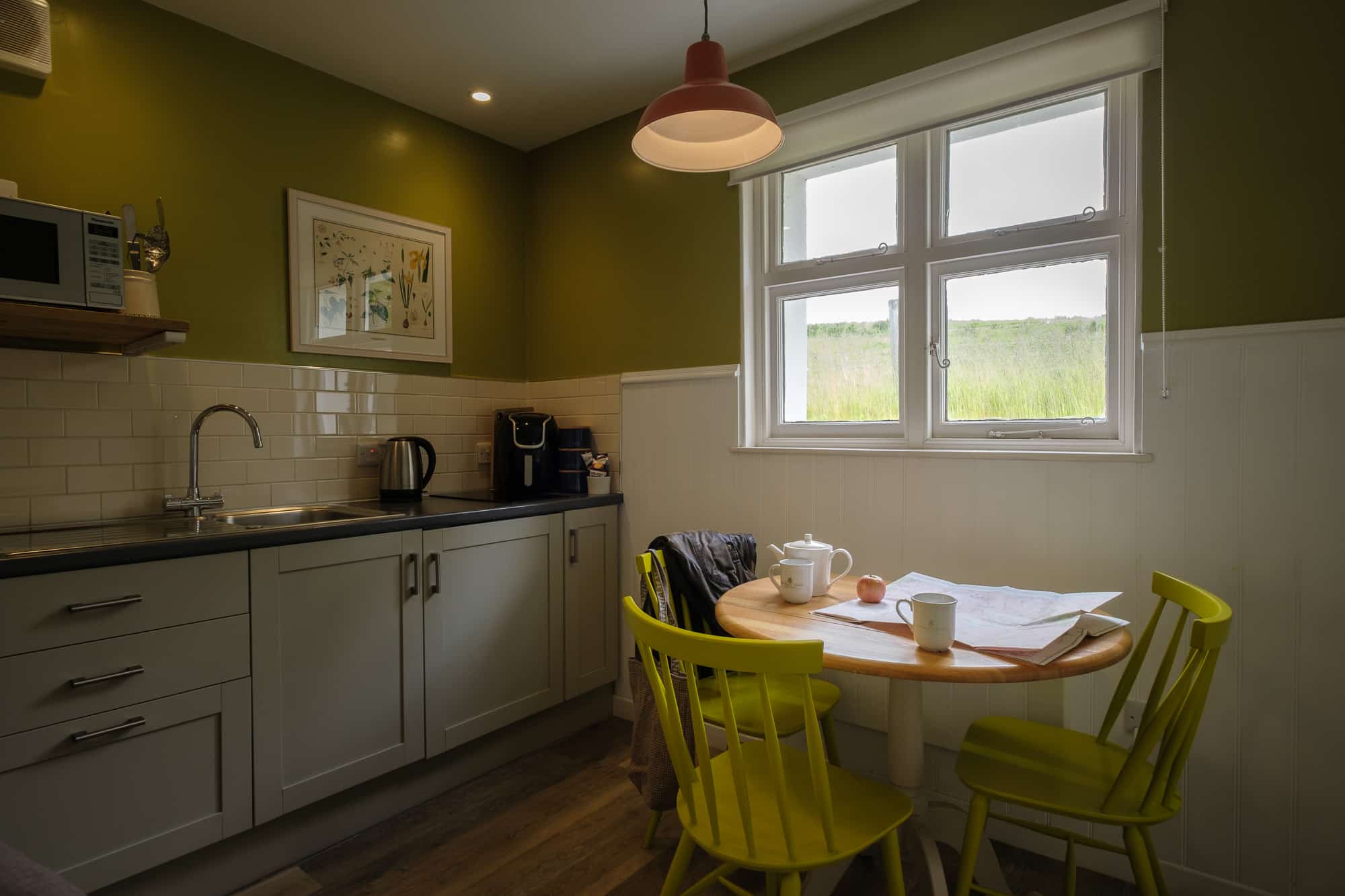 Kitchen_Dining_Dounebrae_Cottage Kitchen and dining area in Dounebrae Cottage with olive feature wall, yellow chairs and countryside view at Douneside House