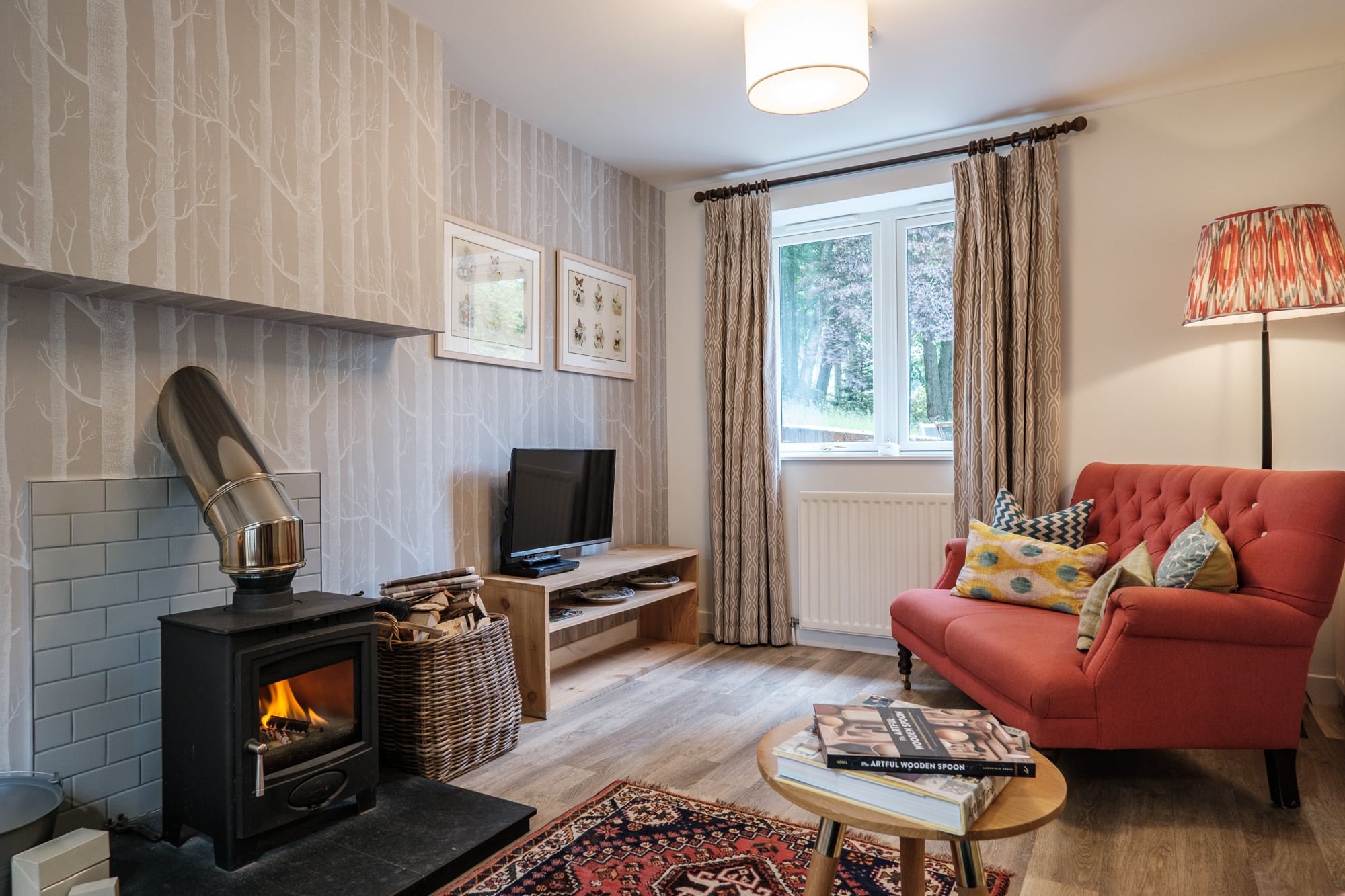 Living room in Casa 23 with red sofa, wood-burning stove and birch tree wallpaper at Douneside House