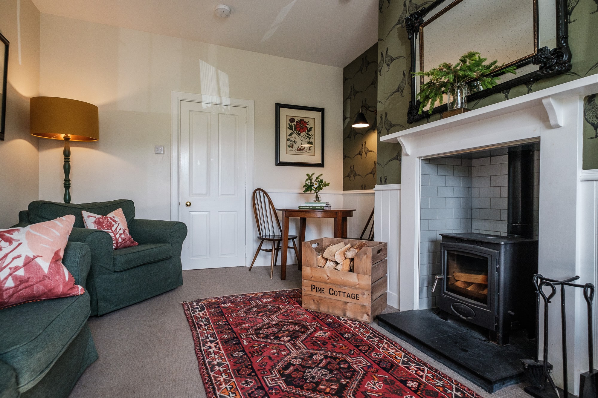 Pine Cottage living room with wood-burning stove, green sofa, log crate and Persian rug at Douneside House