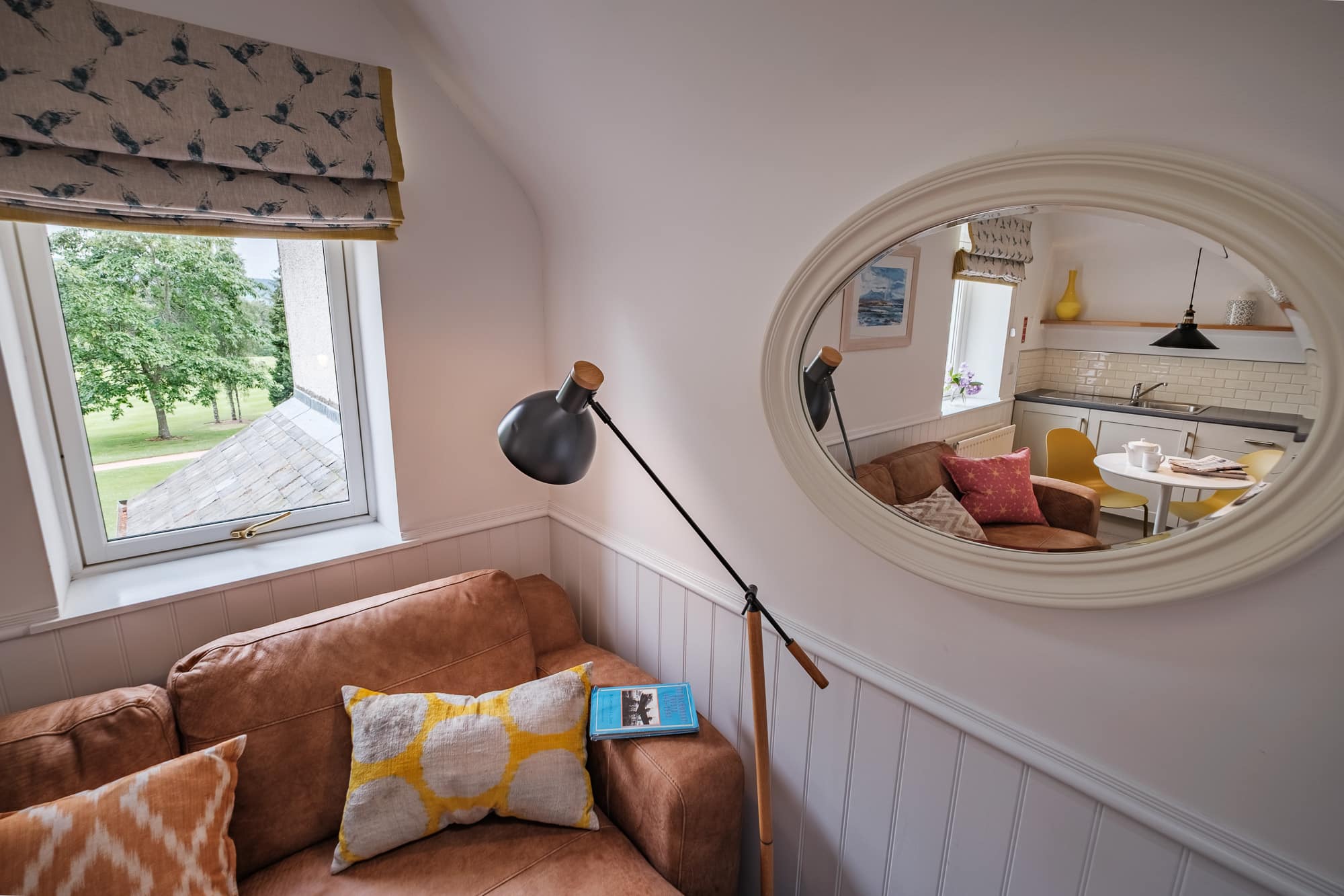 Reading corner in Casa 24 with tan leather sofa, oval mirror and countryside view at Douneside House