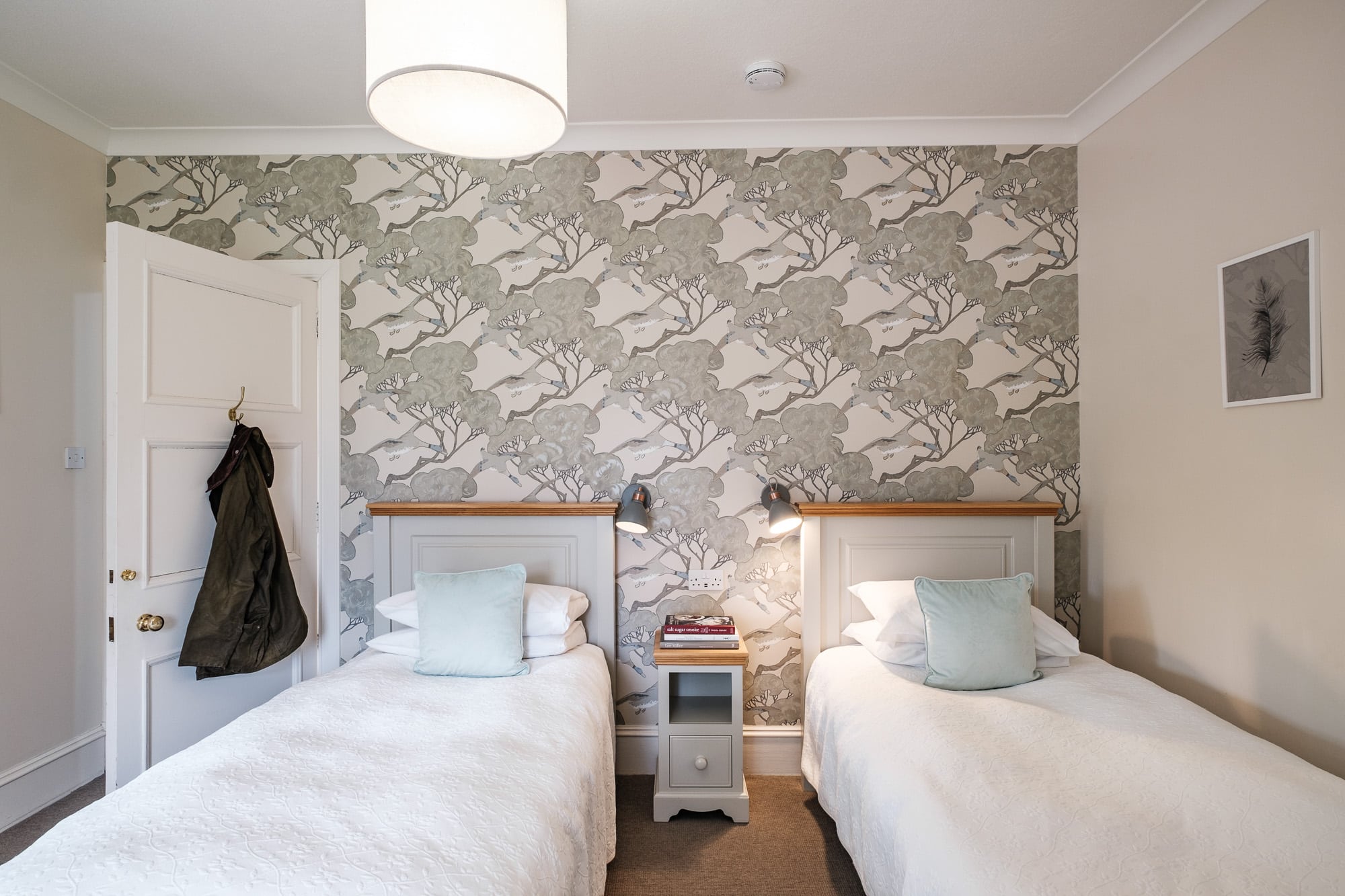 Twin bedroom in Gatehouse with bird print wallpaper, duck-egg cushions and tweed jacket at Douneside House